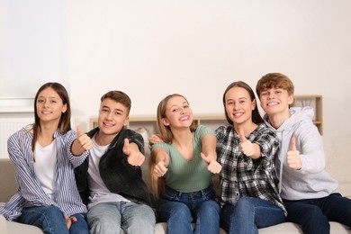 Photo of Group of happy teenagers showing thumbs up while sitting on sofa at home