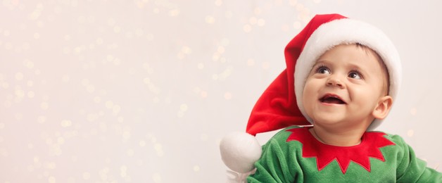 Cute baby wearing Christmas costume against blurred lights, space for text. Banner design