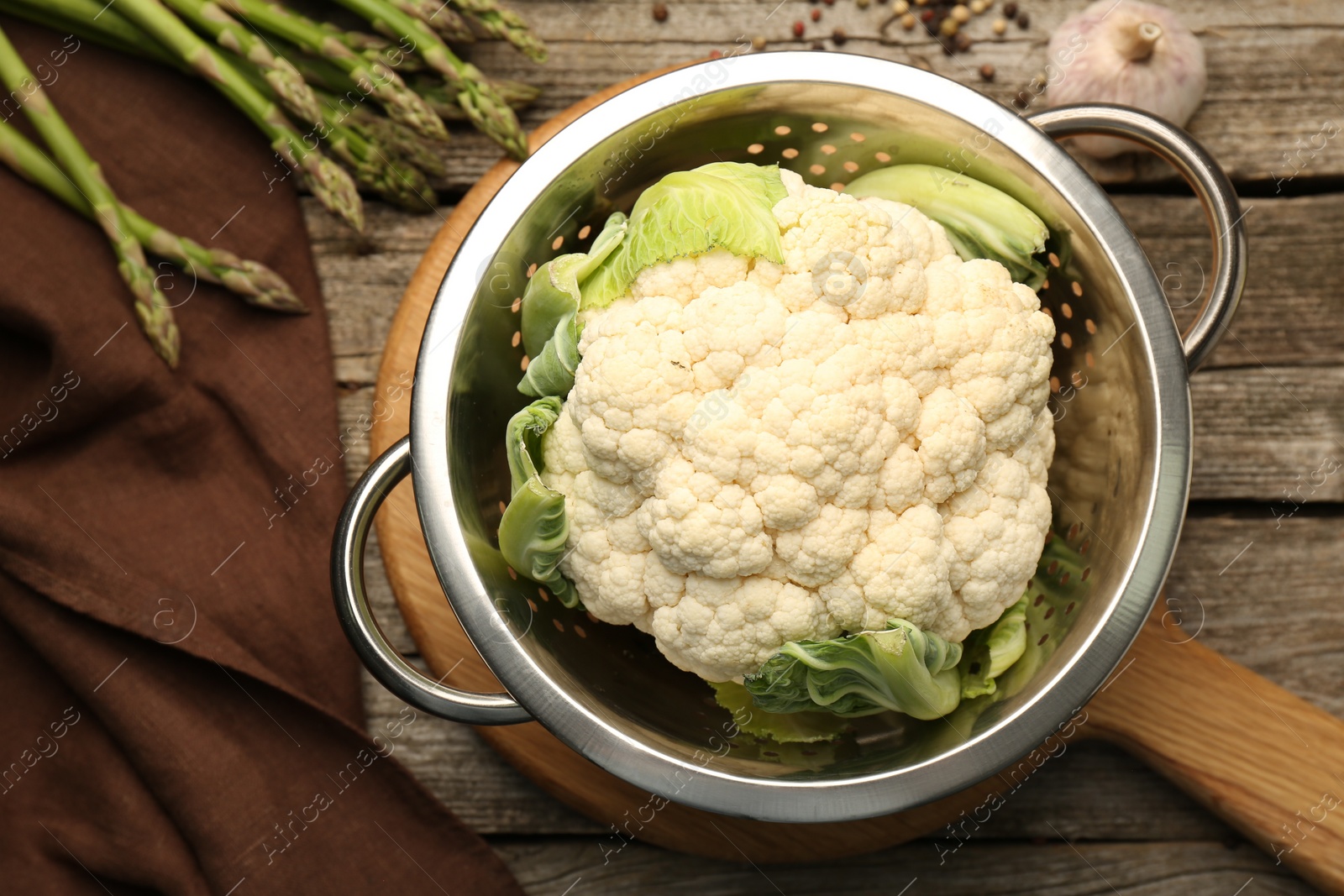 Photo of Metal colander with cauliflower, fennel and asparagus on wooden table, flat lay