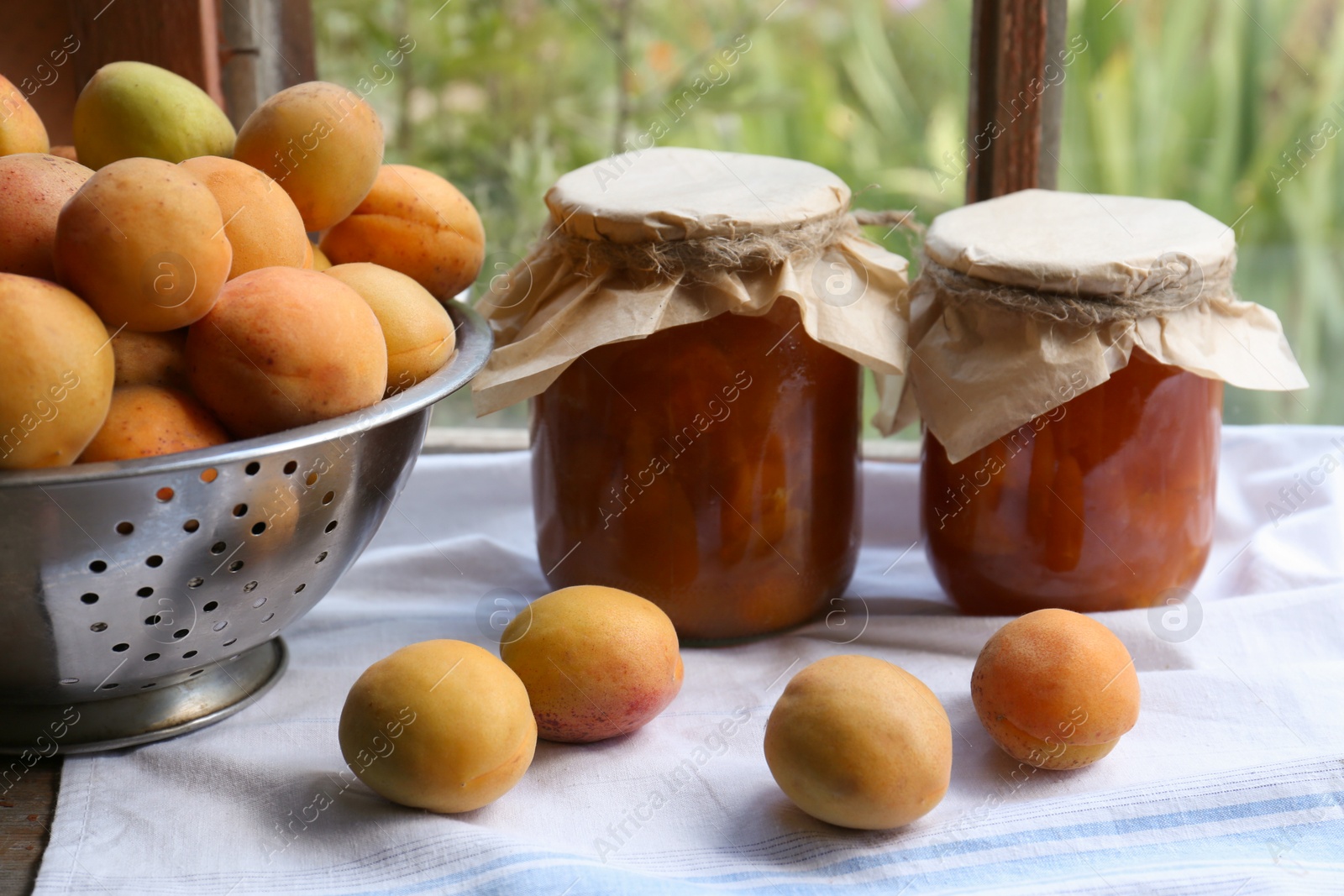 Photo of Delicious ripe apricots with jars of homemade jam on table near window