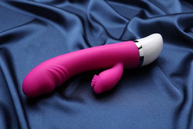 Photo of Pink vaginal vibrator on blue silky fabric. Sex toy