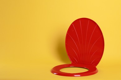 Photo of New red plastic toilet seat on yellow background, space for text