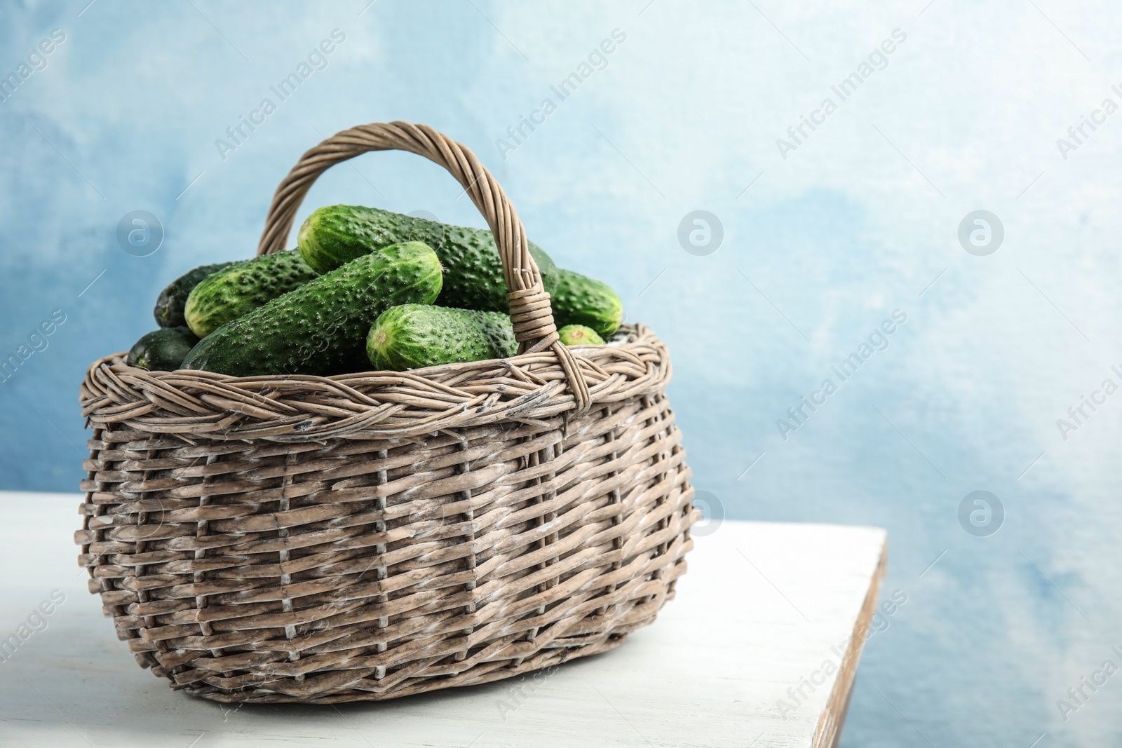 Photo of Wicker basket with ripe fresh cucumbers on table