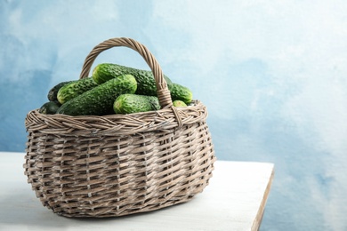 Photo of Wicker basket with ripe fresh cucumbers on table