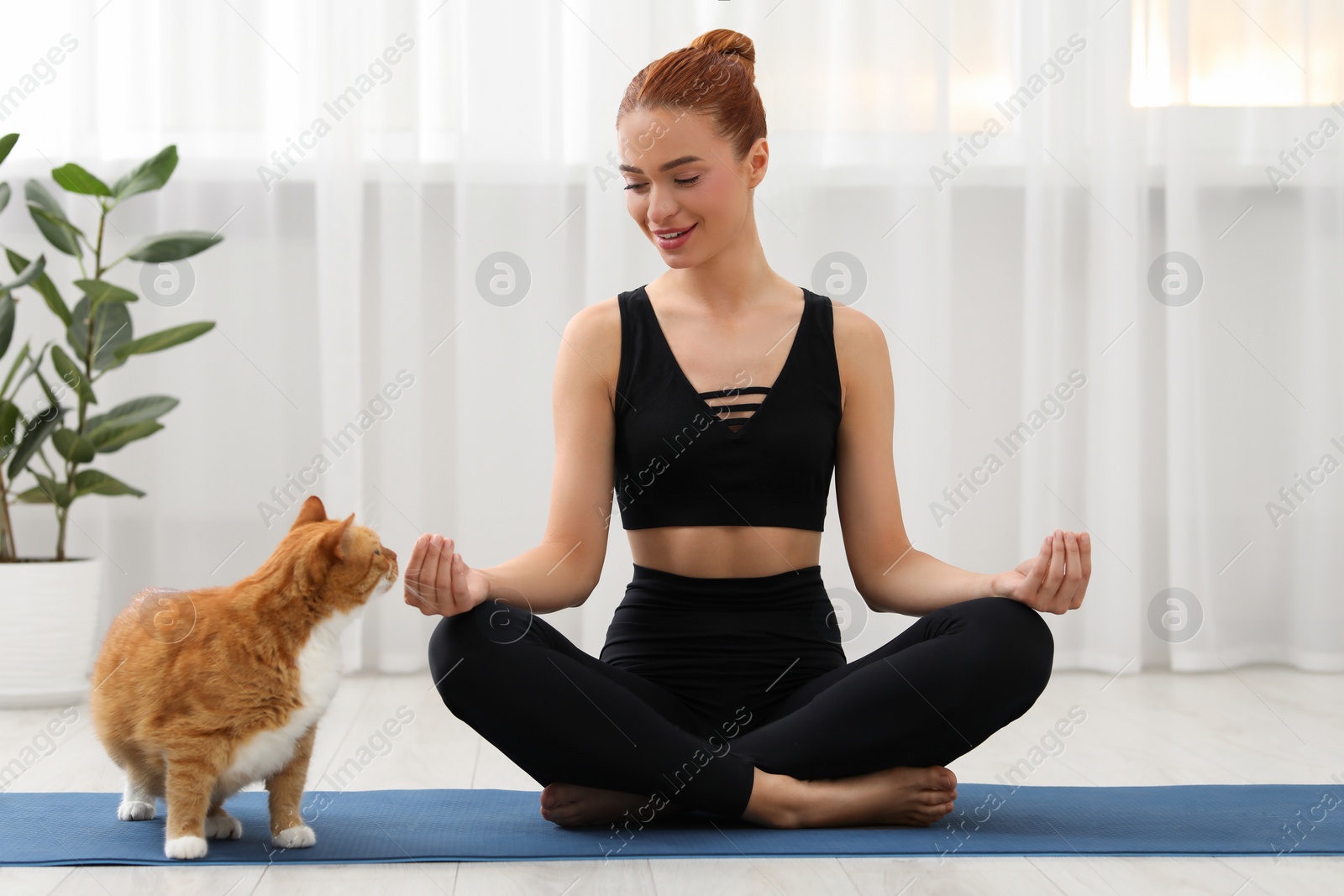 Photo of Beautiful woman with cute red cat practicing yoga on mat at home