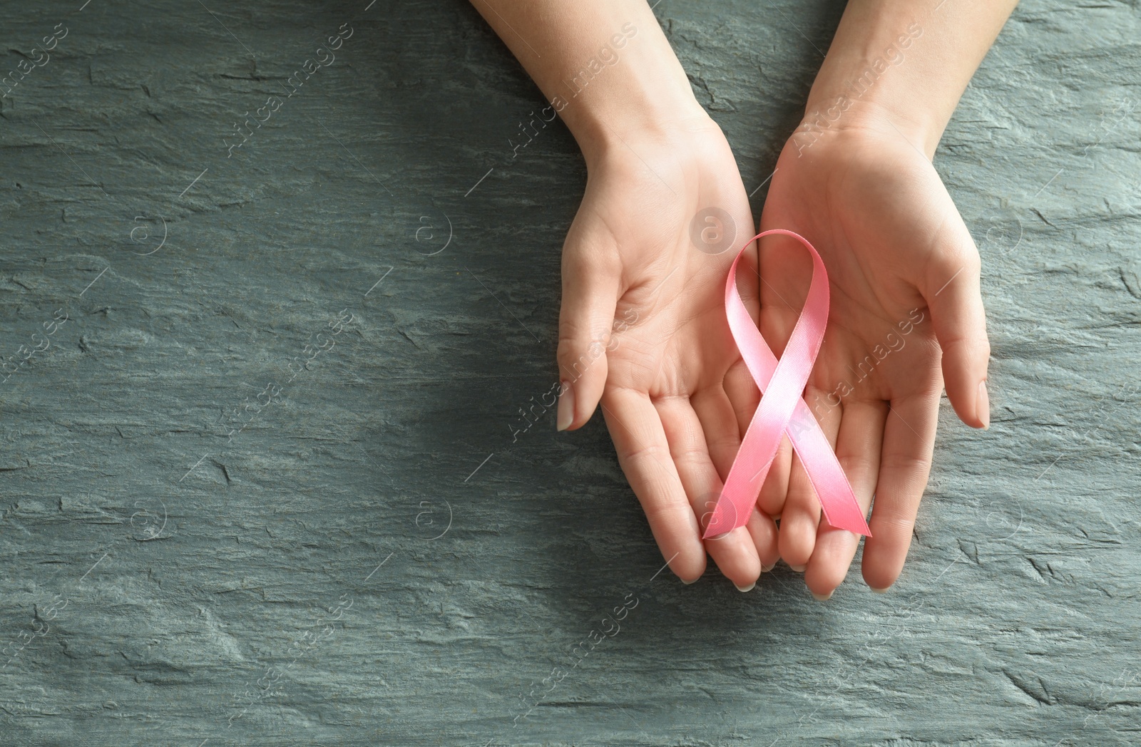 Photo of Woman holding pink ribbon on grey stone background, top view with space for text. Breast cancer awareness