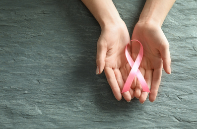 Photo of Woman holding pink ribbon on grey stone background, top view with space for text. Breast cancer awareness