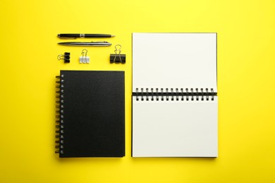 Photo of Notebooks, pens and paper clips on yellow background, flat lay