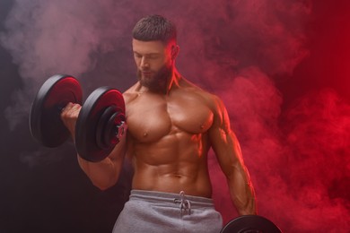 Photo of Young bodybuilder exercising with dumbbells in smoke on color background, low angle view
