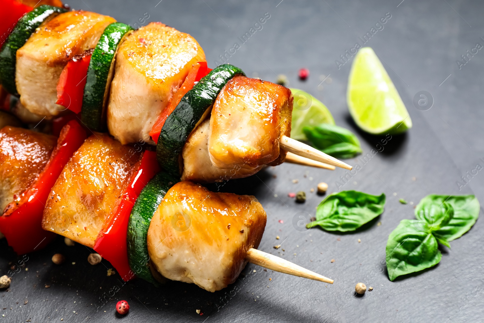 Photo of Delicious chicken shish kebabs with vegetables on black table, closeup