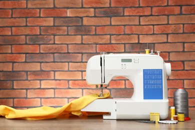 Photo of Sewing machine with fabric and craft accessories on wooden table against brick wall