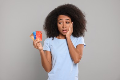 Photo of Confused woman with credit cards on grey background. Debt problem