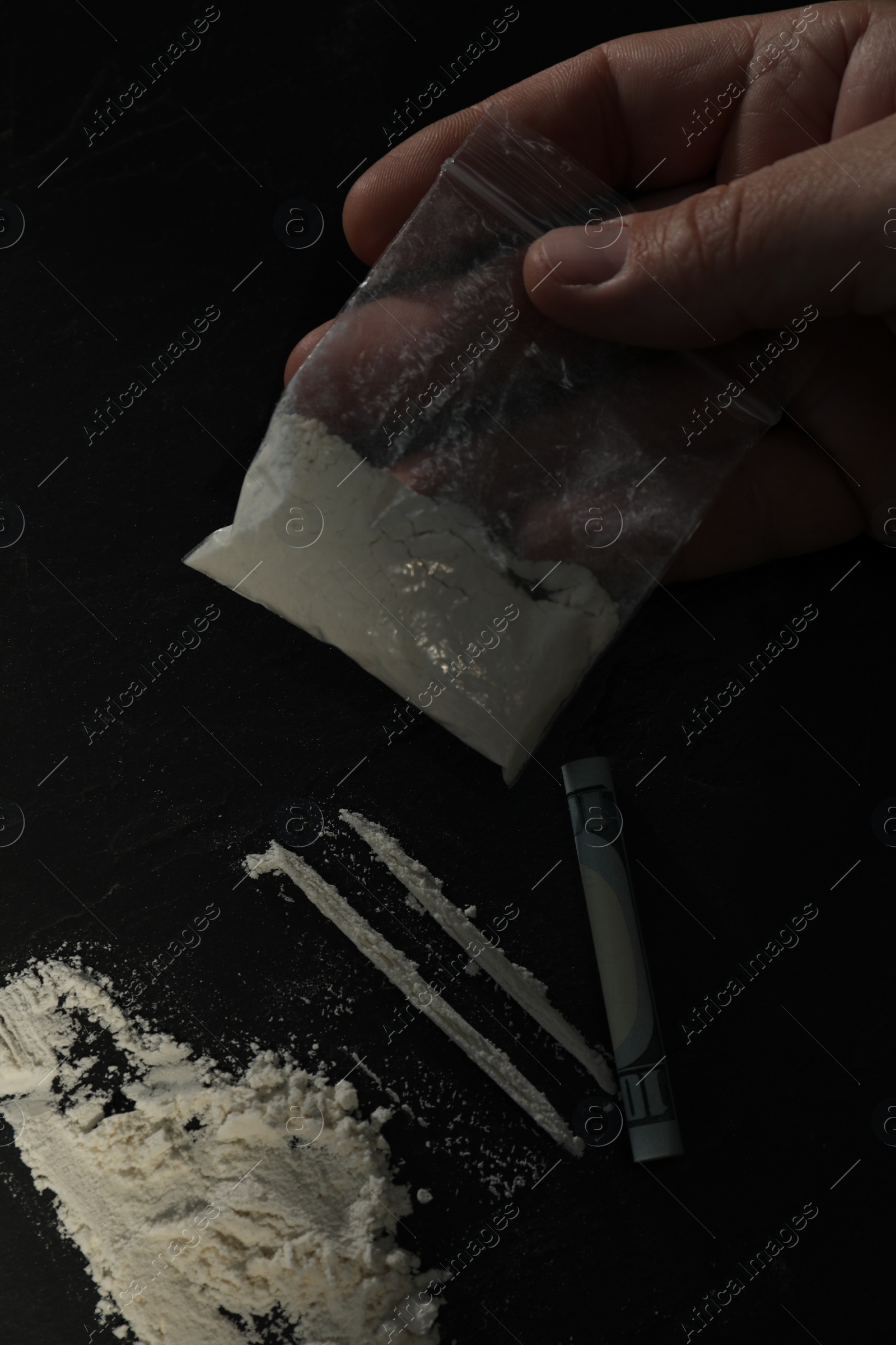 Photo of Drug addiction. Man with cocaine and rolled dollar banknote at dark textured table, closeup