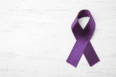 Purple ribbon on white wooden background, top view with space for text. Domestic violence awareness