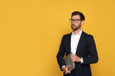 Photo of Portrait of bearded man with glasses and laptop on orange background. Space for text