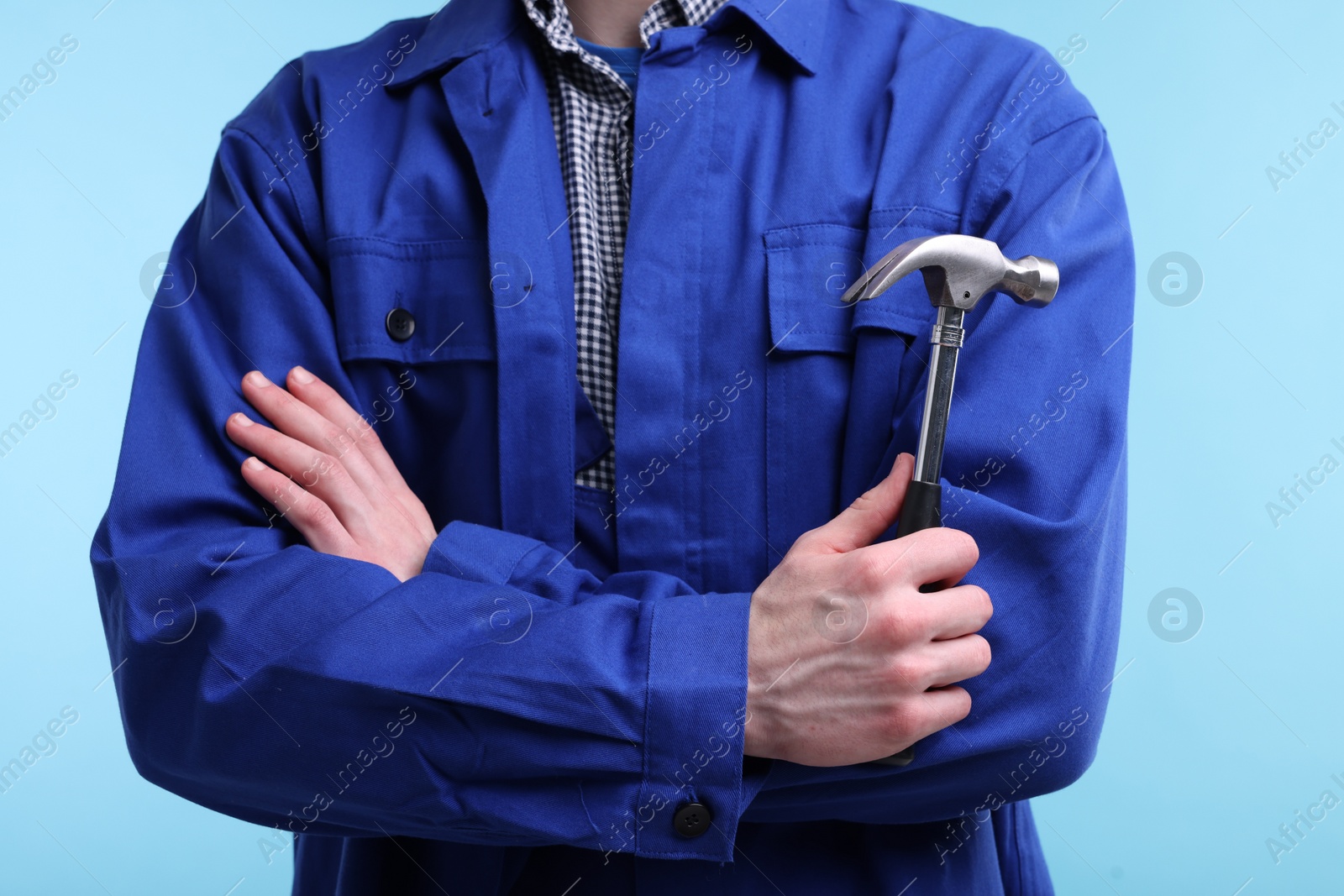 Photo of Professional repairman holding hammer on light blue background, closeup