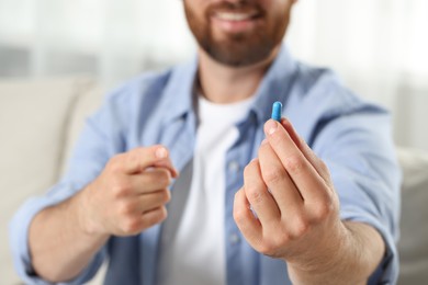 Man showing pill indoors, closeup. Space for text