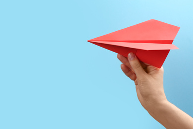 Photo of Woman holding paper plane on light blue background, closeup. Space for text