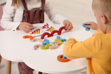 Little children playing with colorful wooden pieces at white table indoors, closeup. Developmental toy