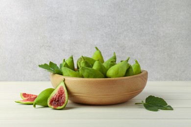 Cut and whole fresh green figs on white wooden table near grey wall, space for text