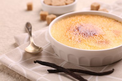 Delicious creme brulee in bowl, vanilla pods and spoon on table, closeup