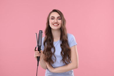 Photo of Happy young woman with beautiful hair holding curling iron on pink background