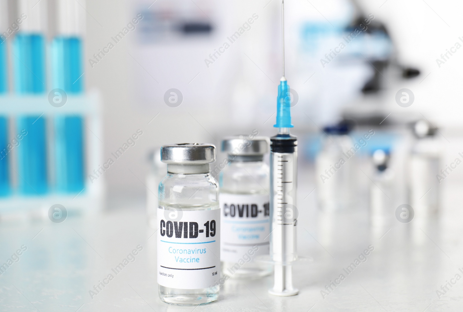 Photo of Vials with vaccine against Covid-19 and syringe on white table indoors