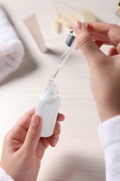 Photo of Woman with bottle and pipette of cosmetic serum at white table, closeup