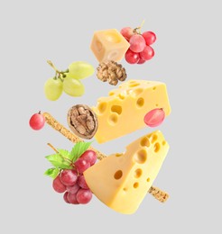 Image of Cheese, breadstick, grapes and walnuts falling against light grey background