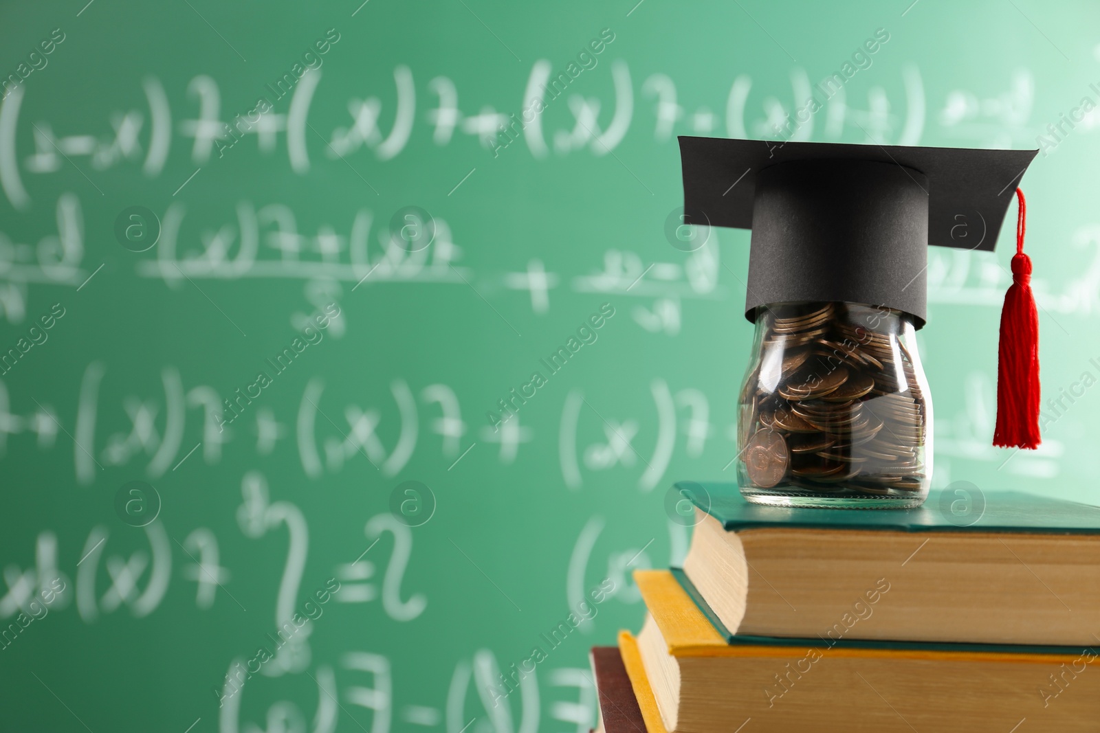 Photo of Scholarship concept. Glass jar with coins, graduation cap and books against greenboard, space for text