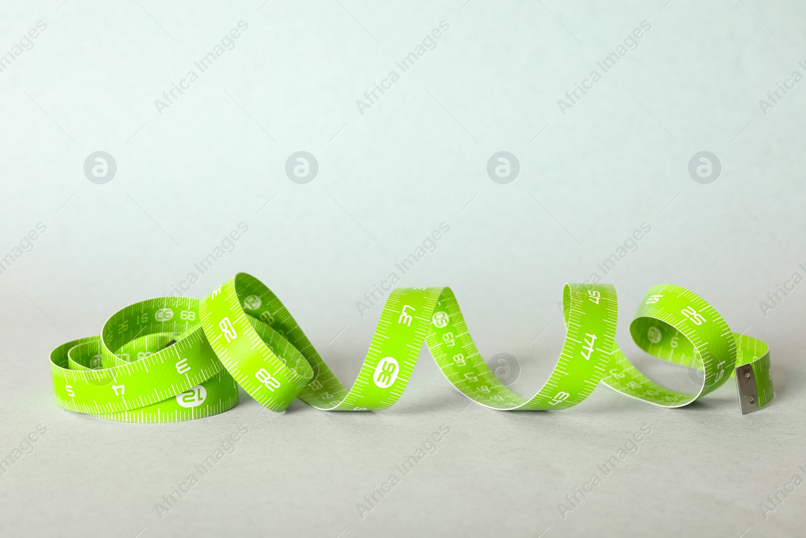 Photo of Green measuring tape on light background, closeup
