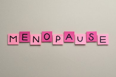 Photo of Pink paper notes with word Menopause on beige background, flat lay