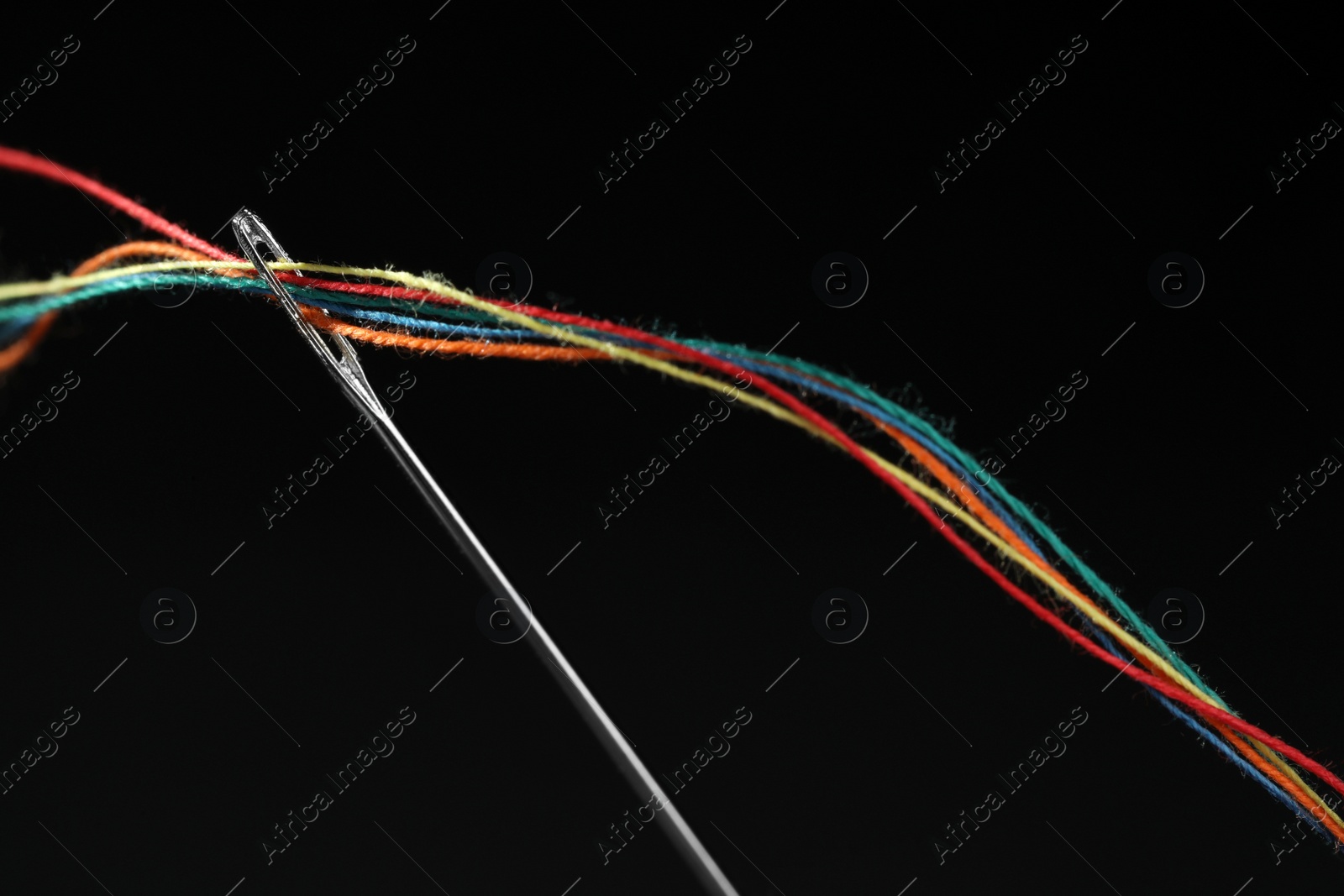 Photo of Sewing needle with colorful threads on black background, closeup