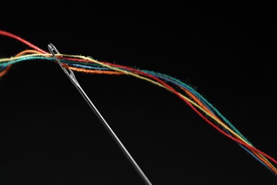 Photo of Sewing needle with colorful threads on black background, closeup