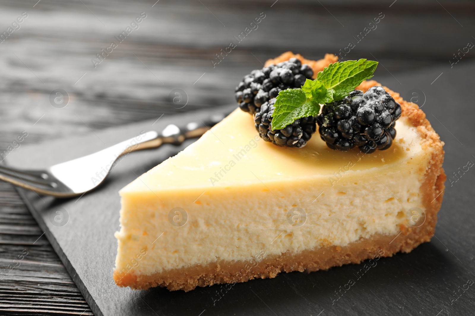 Photo of Piece of delicious cheesecake decorated with blackberries on table