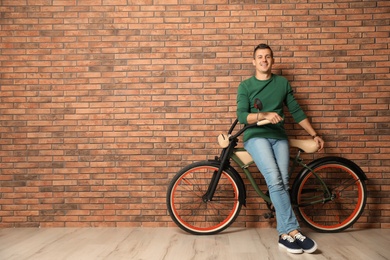 Photo of Portrait of handsome young man with bicycle near brick wall