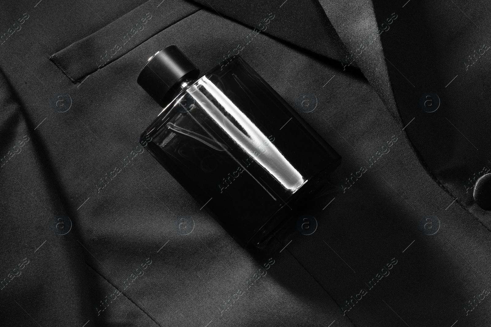 Photo of Luxury men's perfume in bottle on black jacket, top view