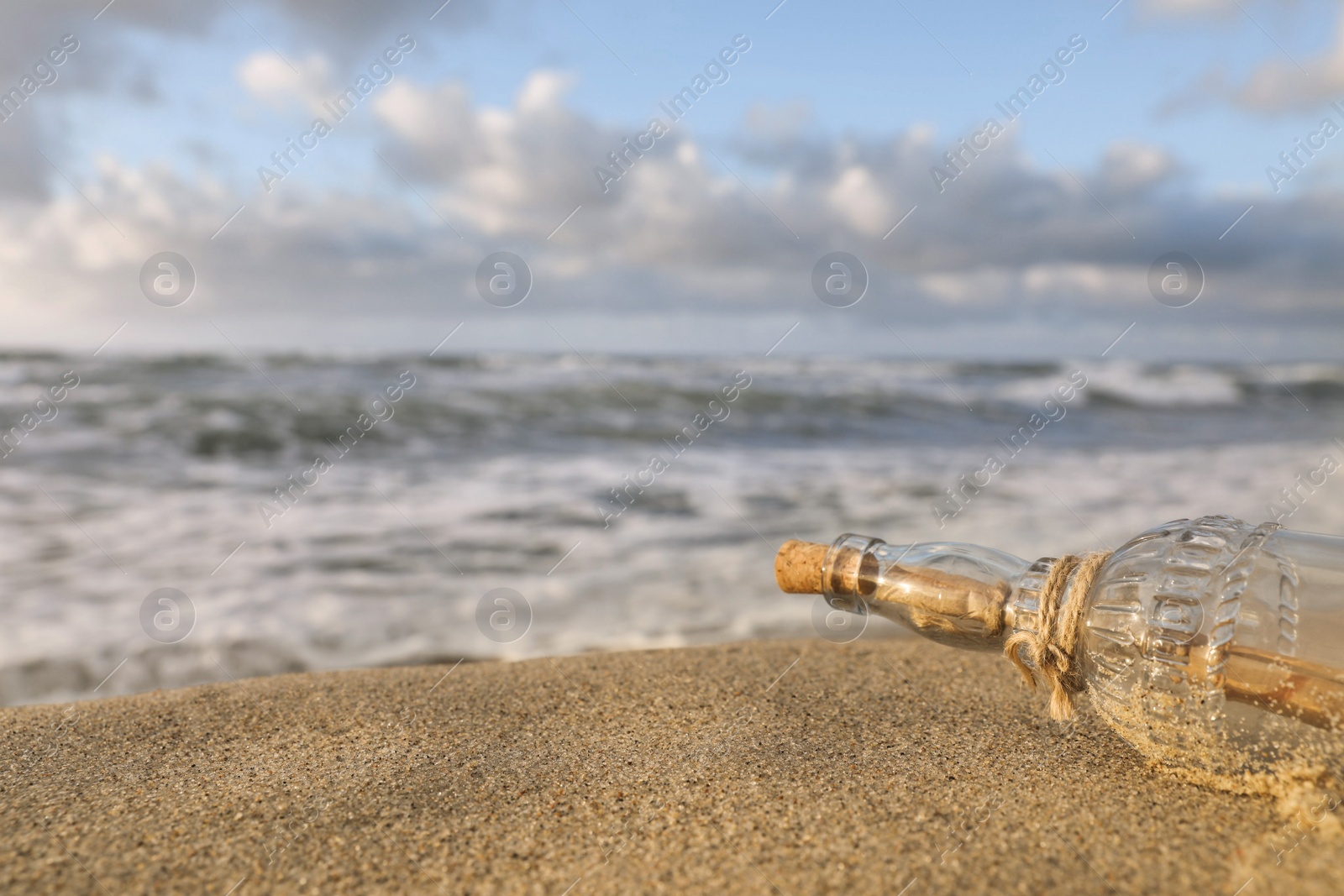 Photo of SOS message in glass bottle on sand near sea, closeup. Space for text