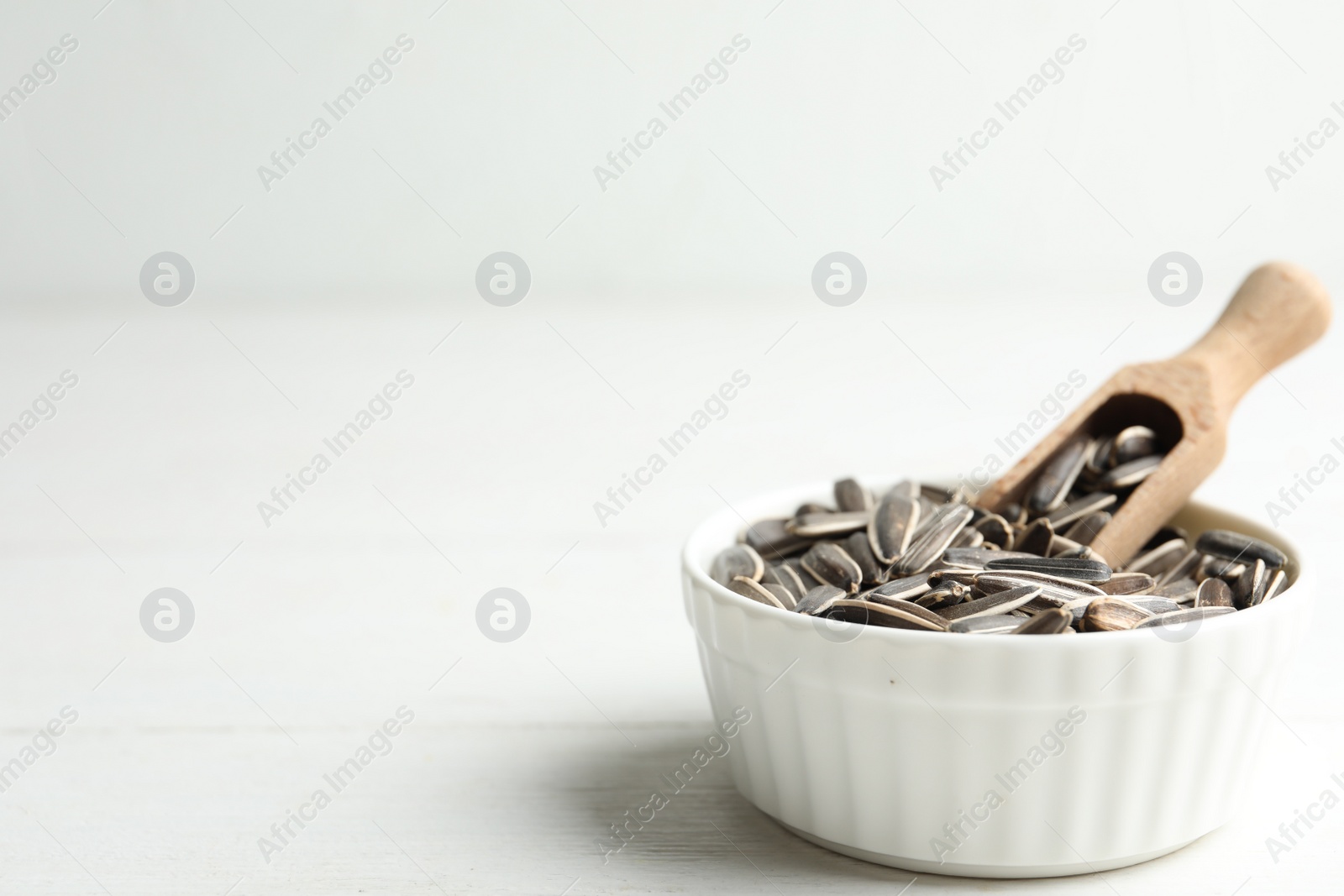 Photo of Organic sunflower seeds on white wooden table. Space for text