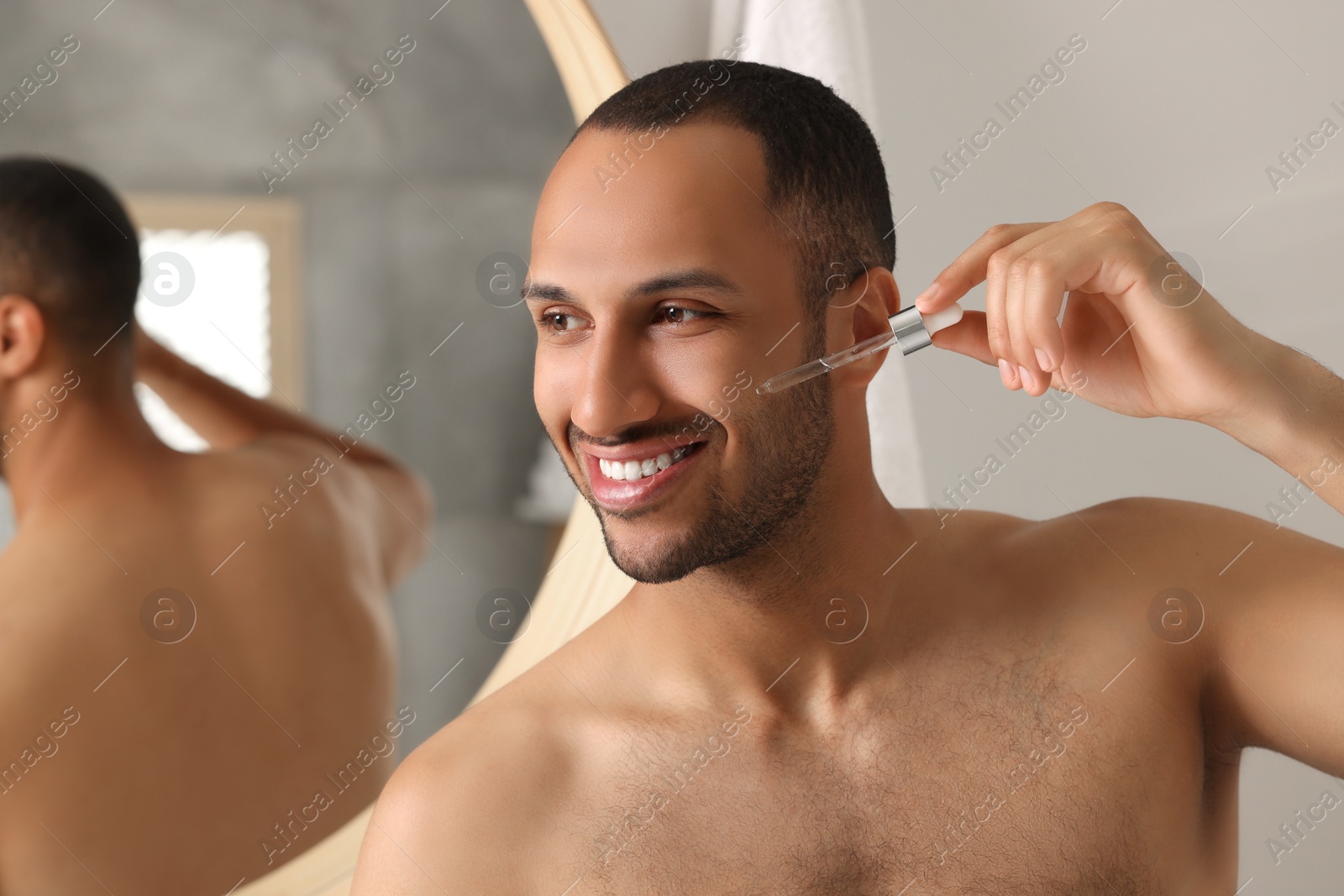 Photo of Handsome man applying cosmetic serum onto face in bathroom, space for text