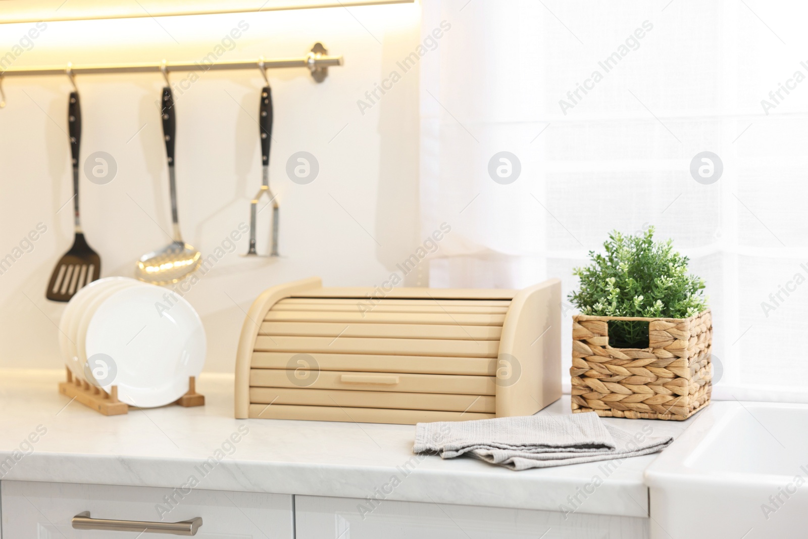 Photo of Wooden bread box, houseplant and plates on white marble countertop in kitchen