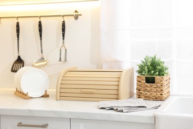 Wooden bread box, houseplant and plates on white marble countertop in kitchen