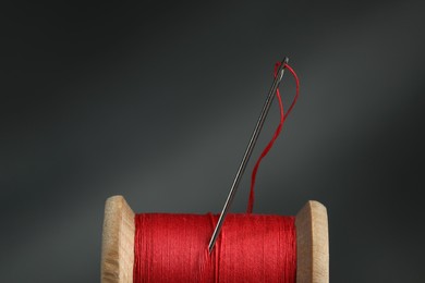 Photo of Red sewing thread with needle on dark background, closeup