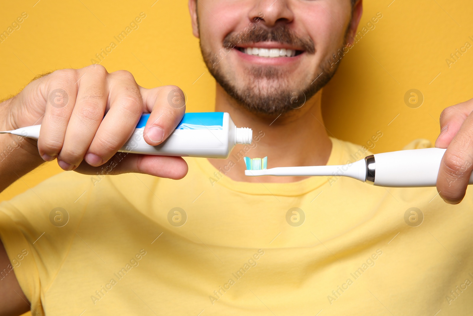 Photo of Young man with electric toothbrush and paste on color background, closeup