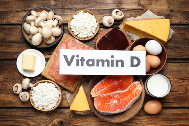 Paper with phrase VITAMIN D and fresh products on wooden table, flat lay