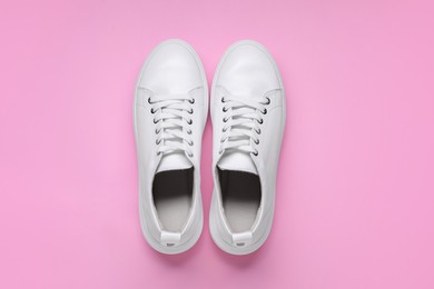 Pair of stylish white sneakers on pink background, top view