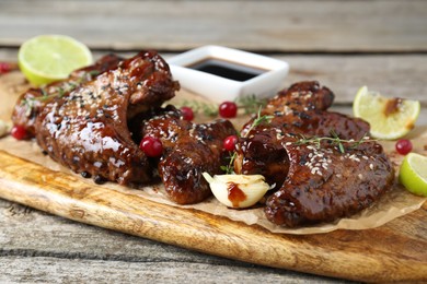 Tasty chicken wings glazed in soy sauce with garnish on wooden table, closeup