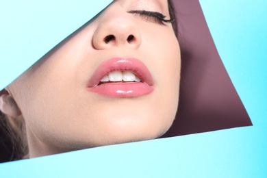 Photo of View of beautiful young woman with perfect lips makeup through cutout in color paper