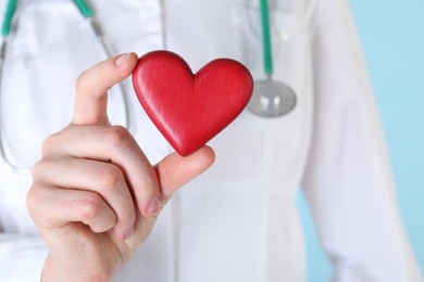 Photo of Doctor with red heart on light blue background, closeup