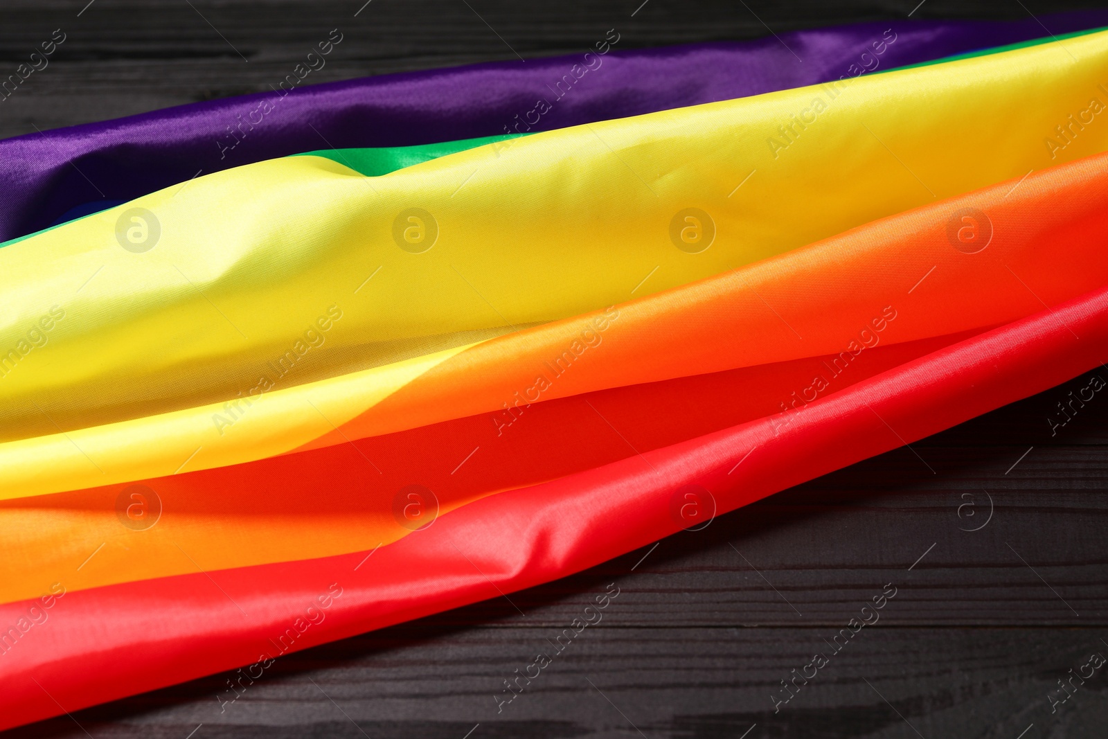 Photo of Rainbow LGBT flag on black wooden background, closeup